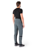 Alpinestars Alden byxor, Urban Gray, sedda bakifrån, tekniska motorcykelbyxor i textil med kviltade detaljer på den övre bakre linningen och benen, kombinerade med ett svart baslager och grå motorskor, modern urban streetwear-stil.