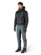 Alpinestars Alden-byxor i Urban Gray, bärs av en modell med en svart kviltad jacka med huva, handskar och motorskor, med kviltade detaljer på sidorna och svarta paneler på innerbenen, streetwear-inspirerad urban motorcykelutrustning.