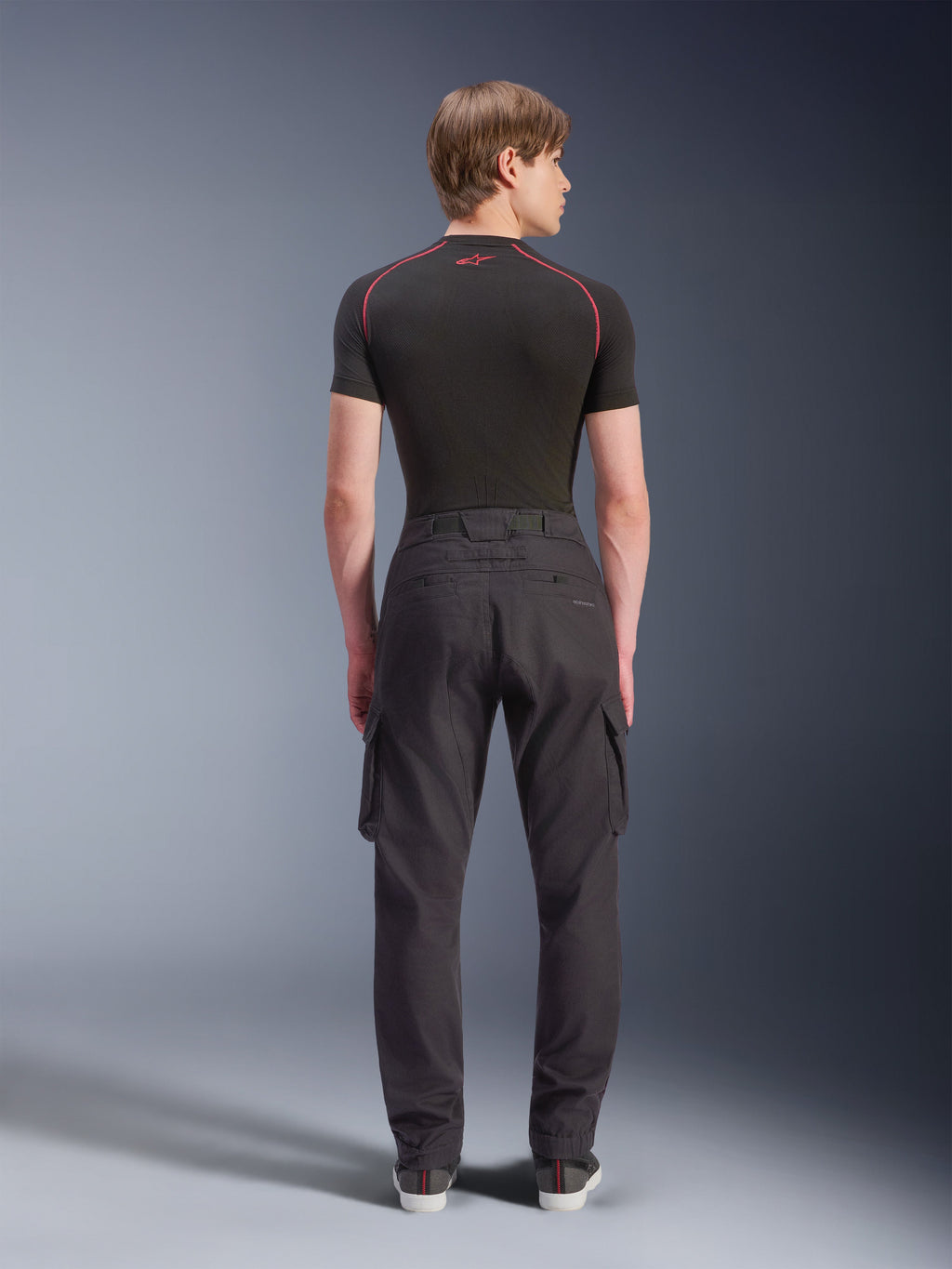 Alpinestars Flex-AST Cargo Pants - Short, svarta urbana motorcykelbyxor sedda bakifrån, med cargofickor på sidorna och elastiska benslut, bärs med ett svart kortärmat underställ med röda kontrastsömmar
