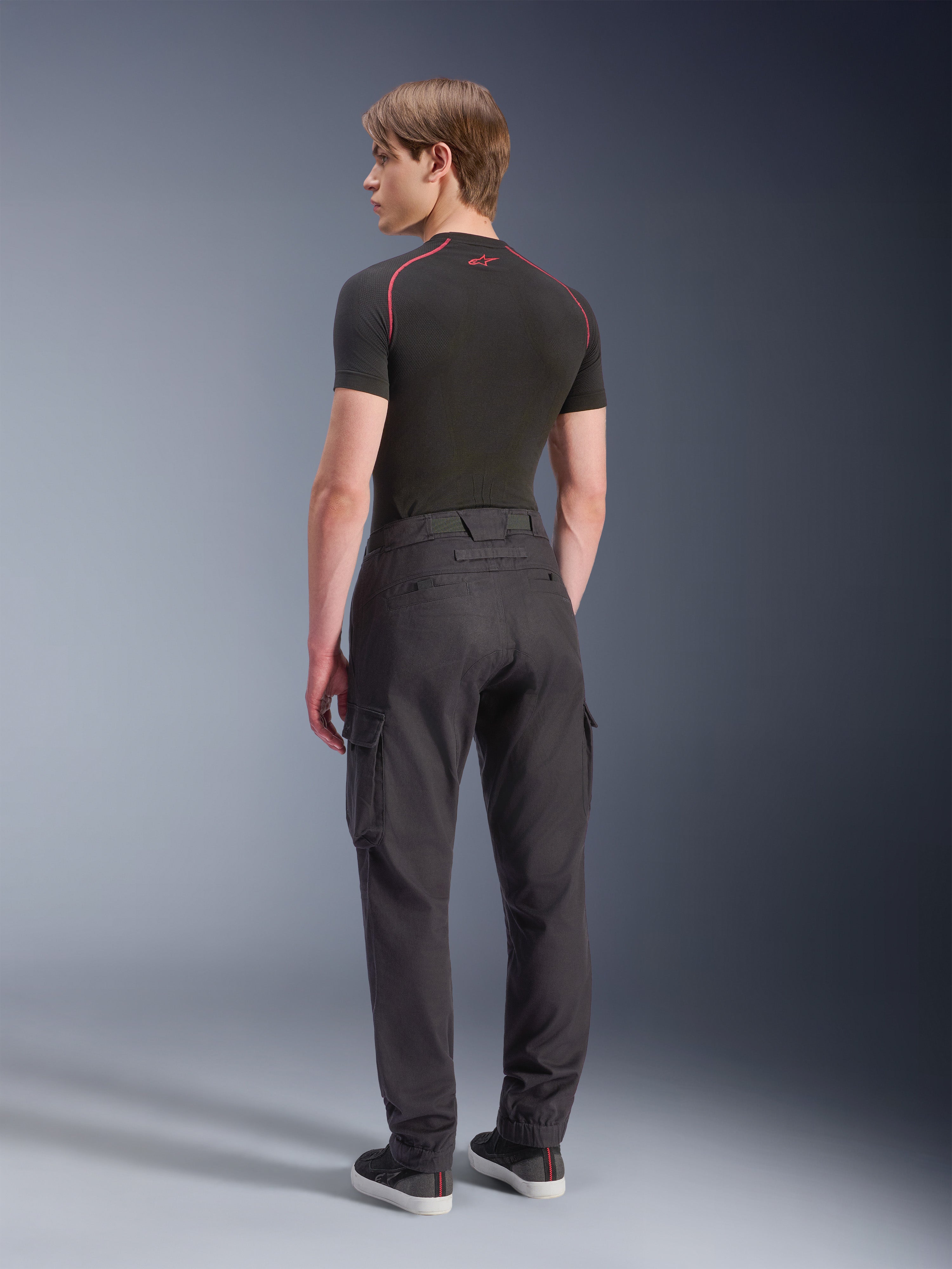 Alpinestars Flex-AST Cargo Pants - Short, motorcykelcargobyxor, svarta, baksida av modell som bär regular tapered cargobyxor med sidofickor och elastiska benslut, kombinerat med ett svart baslager och vardagsskor