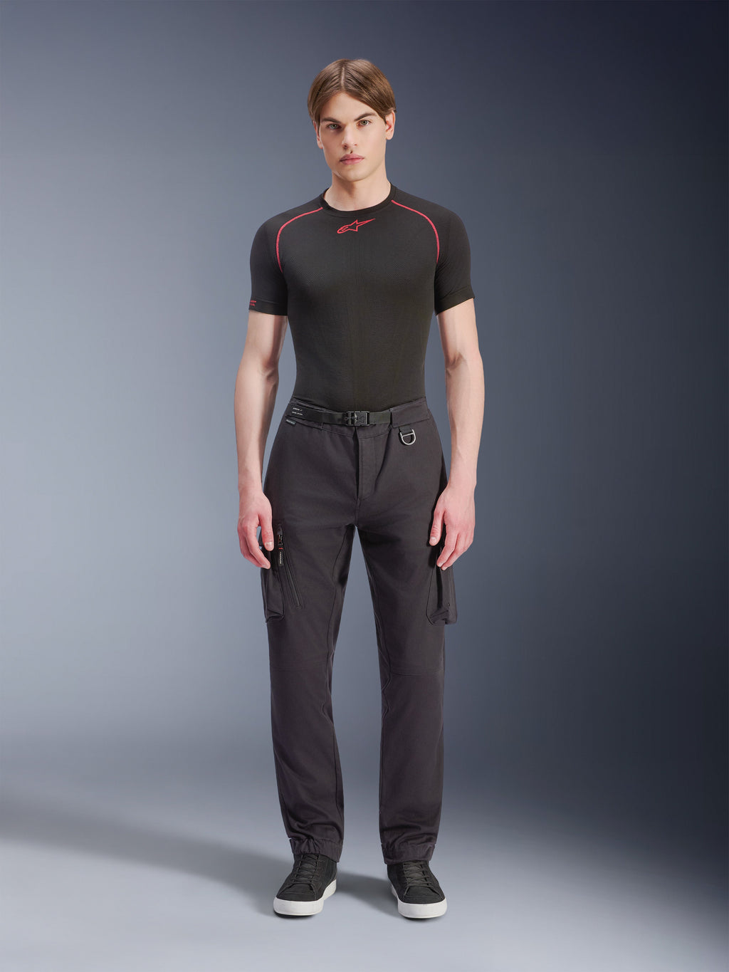 Alpinestars Flex-AST Cargo Pants - Short, svarta, bärs av en manlig modell med en svart funktionströja och svarta sneakers, urbana motorcykelbyxor med flera cargofickor, en avsmalnande passform och ett inbyggt bälte med spänne och D-ring