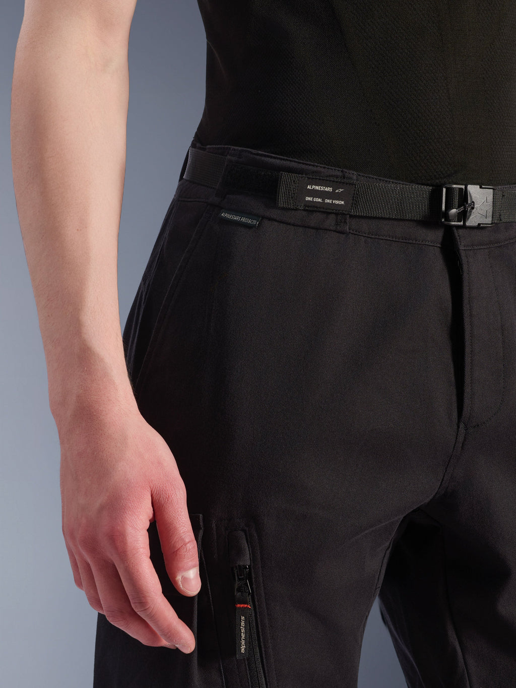 Alpinestars Flex-AST Cargo Byxor, urbana motorcykelbyxor, svarta, närbild på midja och sidoficka, med ett integrerat bälte med Alpinestars-märkning, spänne och en dragkedjeficka med märkt dragkläpp, teknisk textilkonstruktion för urban körning