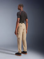 Alpinestars Flex-AST Cargo Pants, urbana motorcykelbyxor, ljusbeige, visas från en vinkel snett bakifrån, med funktionella cargofickor och elastiska benslut, matchas med en svart kortärmad tröja och svarta sneakers.