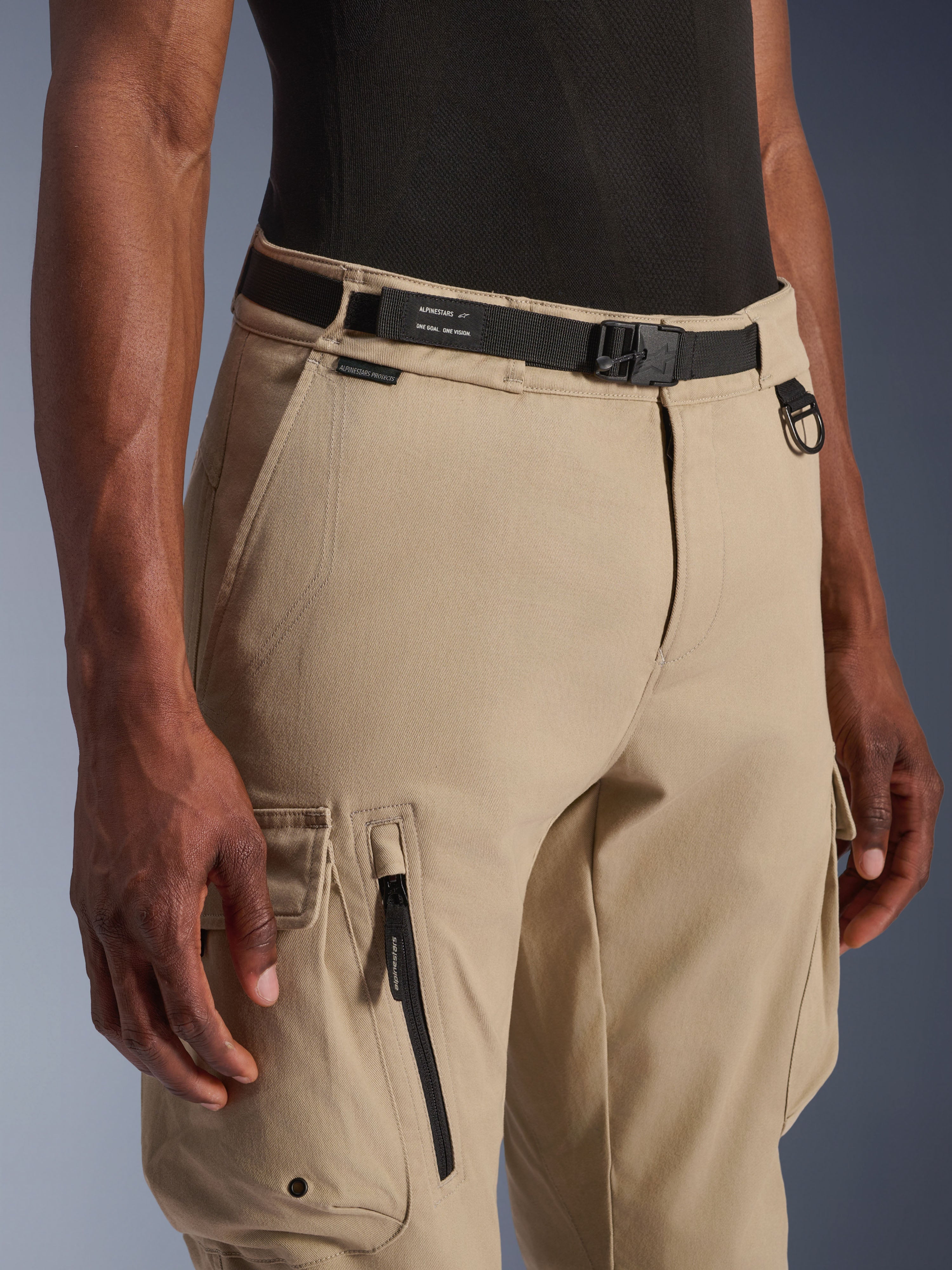 Alpinestars Flex-AST Cargo Pants - Short, ljusbeige, närbild av midja och lår, med ett svart justerbart bälte med Alpinestars-märkning, D-ring i metall och funktionella cargofickor med dragkedjor och lock med tryckknappar, urban modern motorcykelutrustning