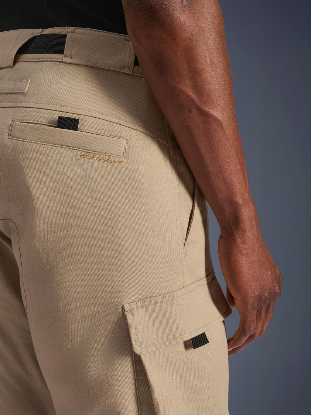 Alpinestars Flex-AST Cargo Pants, ljusbeige, närbild på höft- och sidocargofickor, med broderad märkeslogotyp, svarta dragflikar och militärinspirerad twill-design för urbana motorcyklister