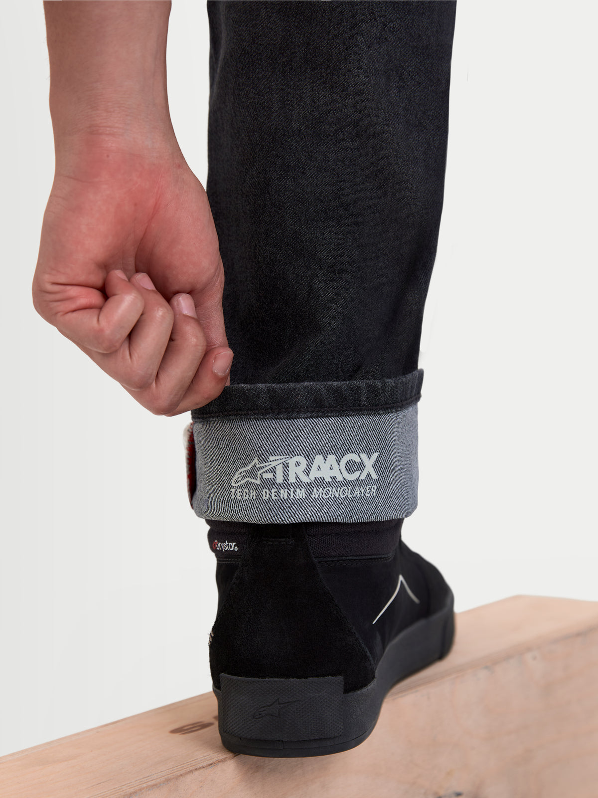 Alpinestars Flex-AST 8 denimbyxor, urbana motorcykeljeans i svart, närbild på det uppvikta benet som visar A-TRAACX teknisk denimkonstruktion i ett lager och invändig märkning