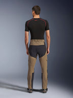 Alpinestars Flex-AST Explorer-byxor, Walnut Black, sedda bakifrån på modell, med förstärkt svart säte och brunt stretchmaterial, kombinerade med svart baslager och tekniska motorcykelstövlar, slitstark utrustning för äventyrskörning