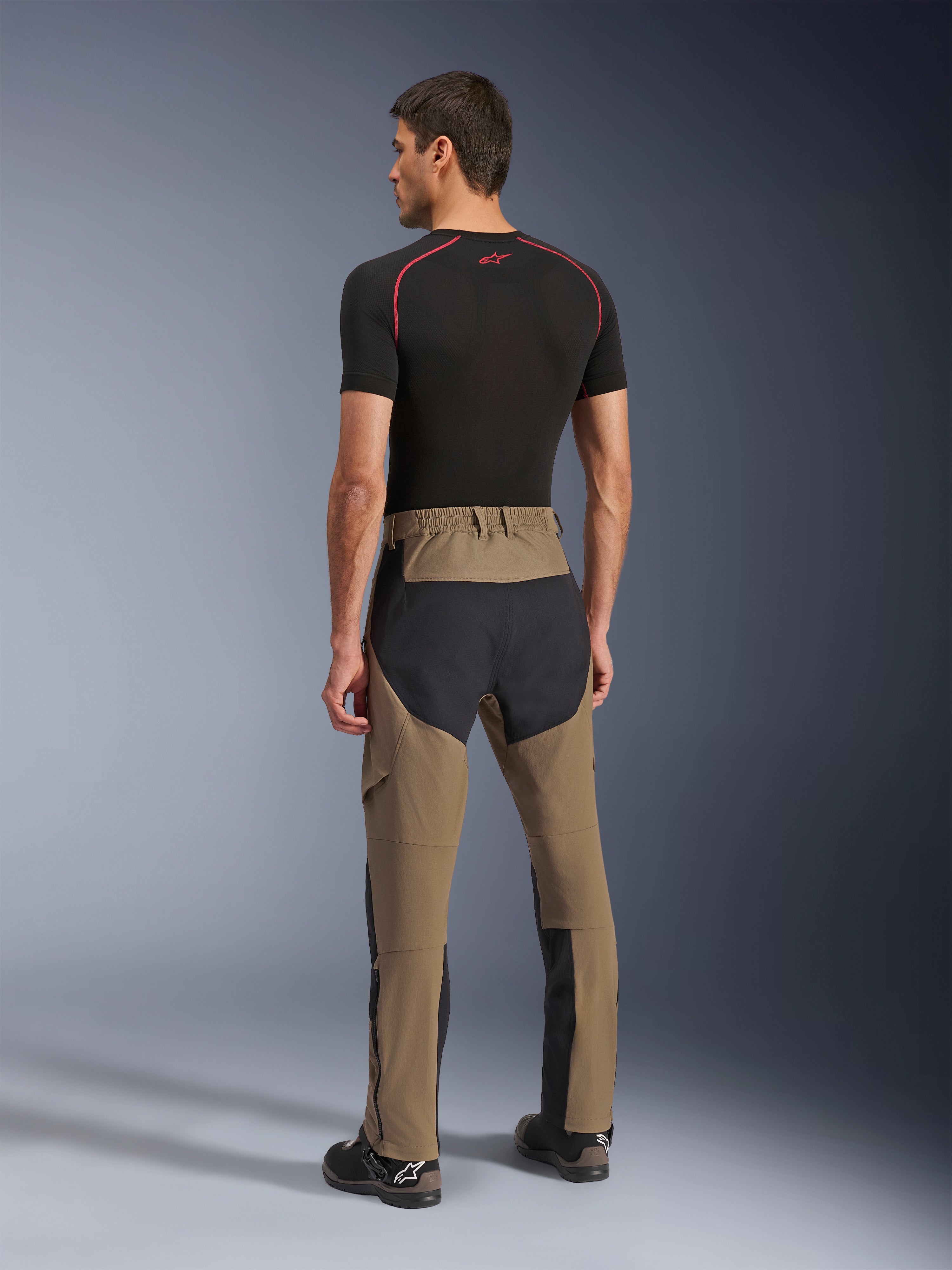 Alpinestars Flex-AST Explorer-byxor, äventyrsmotorcykelbyxor, Walnut Black, baksida på modell som visar svarta ripstop-paneler på säte och ben, stretchtextilkonstruktion och långa dragkedjor på underbenen för äventyrstouring