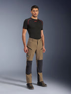 Alpinestars Flex-AST Explorer Pants, Walnut Black äventyrsbyxor för motorcykel, bärs av en manlig modell med ett svart kortärmat underställ och äventyrsstövlar, utrustade med cargofickor med dragkedja och förstärkta knäpaneler, teknisk utrustning för dual-sport- och touringförare.