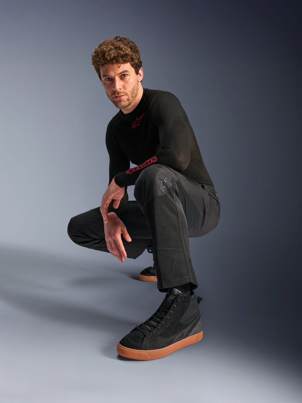 Alpinestars C-1 Air Pants, Urban Motorcycle Pants, Black, model crouching in a studio setting, worn with a black long-sleeve top and black sneakers with tan soles, featuring breathable mesh panels and a contemporary urban style