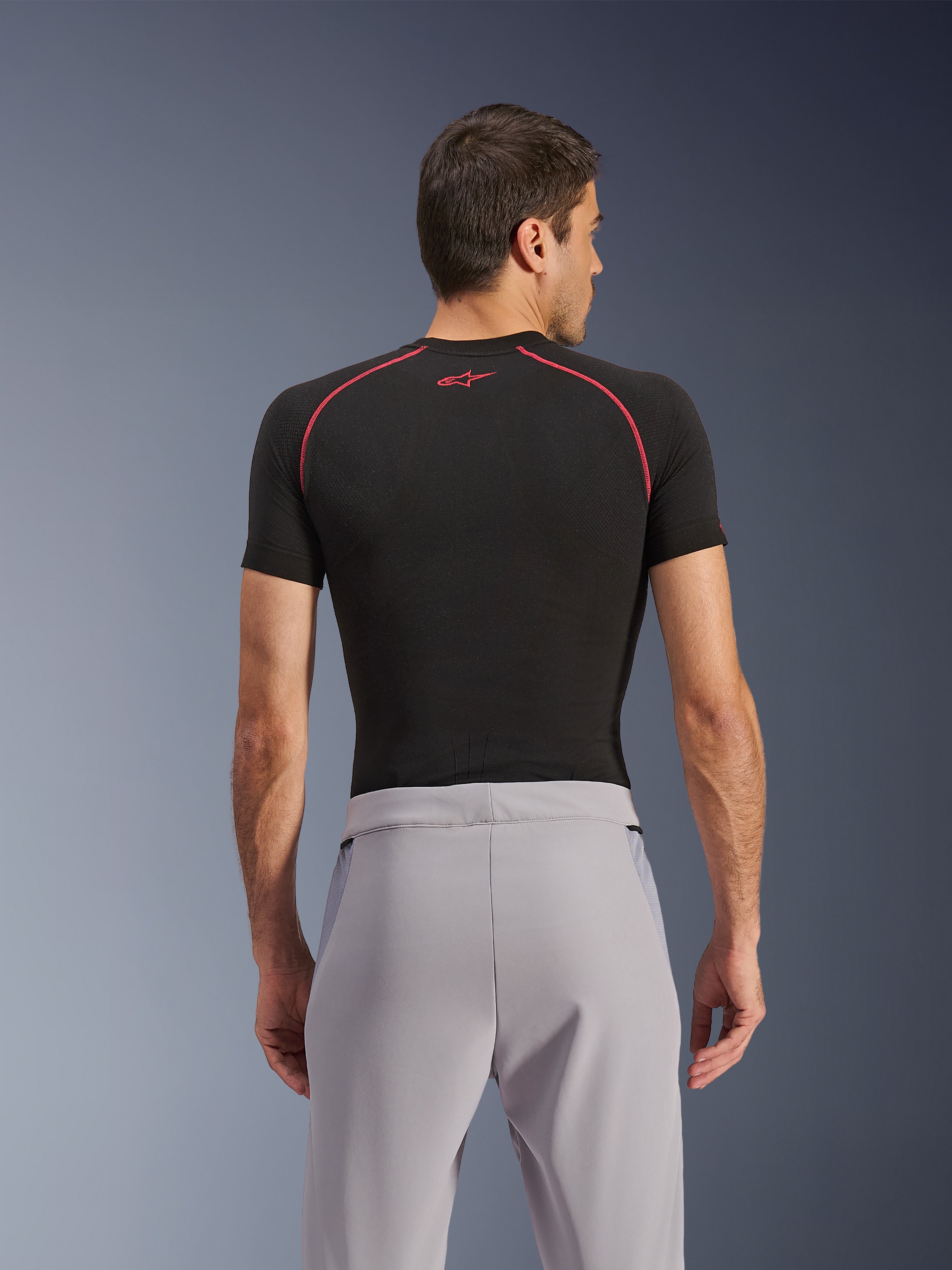 Alpinestars Aeroshell Airflow byxor, Mid Gray, vy bakifrån, bärs med ett svart kortärmat underställ med röda sömmar och logotyp, med lätt stretch-softshell och meshpaneler för maximal ventilation, ergonomisk sportpassform för motorcykelkörning