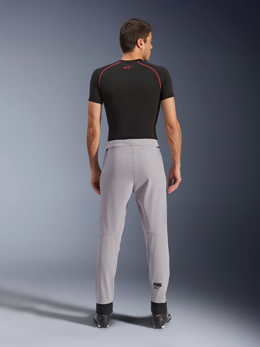 Alpinestars Aeroshell Airflow byxor, Mid Gray, vy bakifrån som visar laserperforerade zoner på vaderna, lätt konstruktion i stretch-softshell, bärs med en svart kortärmad tröja och motorcykelstövlar, sport-fit-design för körning i varmt väder
