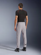 Bakifrån av en modell som bär Alpinestars Aeroshell Airflow-byxor i Mid Gray, kombinerat med en svart underställströja och svarta skor, vilket framhäver de laserperforerade zonerna på vaderna och den atletiska sportpassformen.