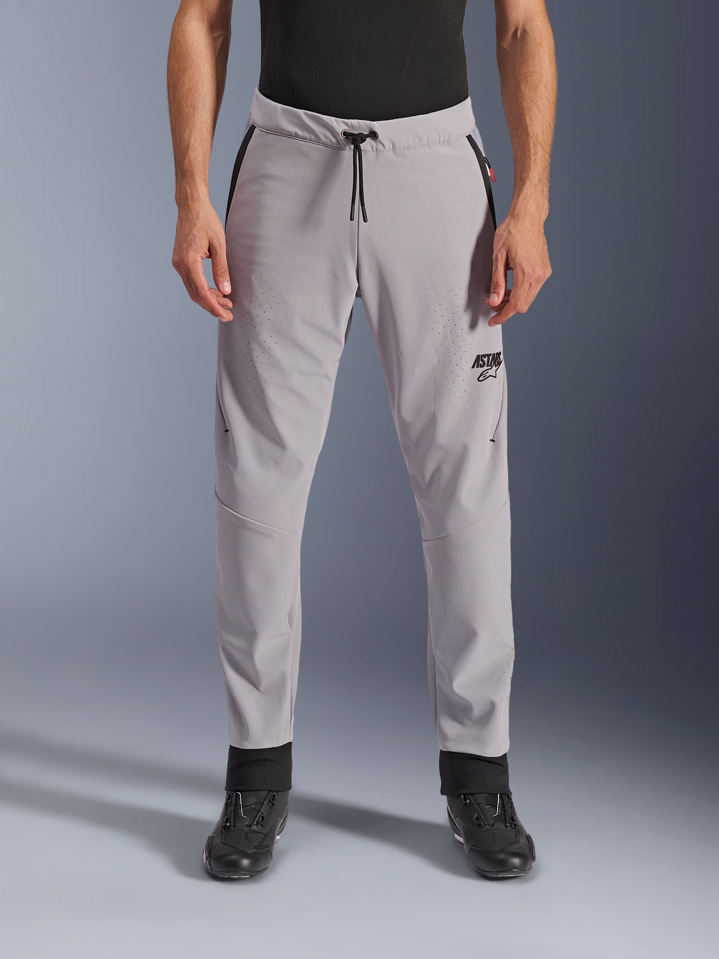 Alpinestars Aeroshell Airflow byxor, mellangrå, vy framifrån som visar laserperforerade zoner på lår och smalben, svart dragsko i midjan och svart ASTARS-logotyp, lättviktigt softshell-chassi för körning i varmt väder