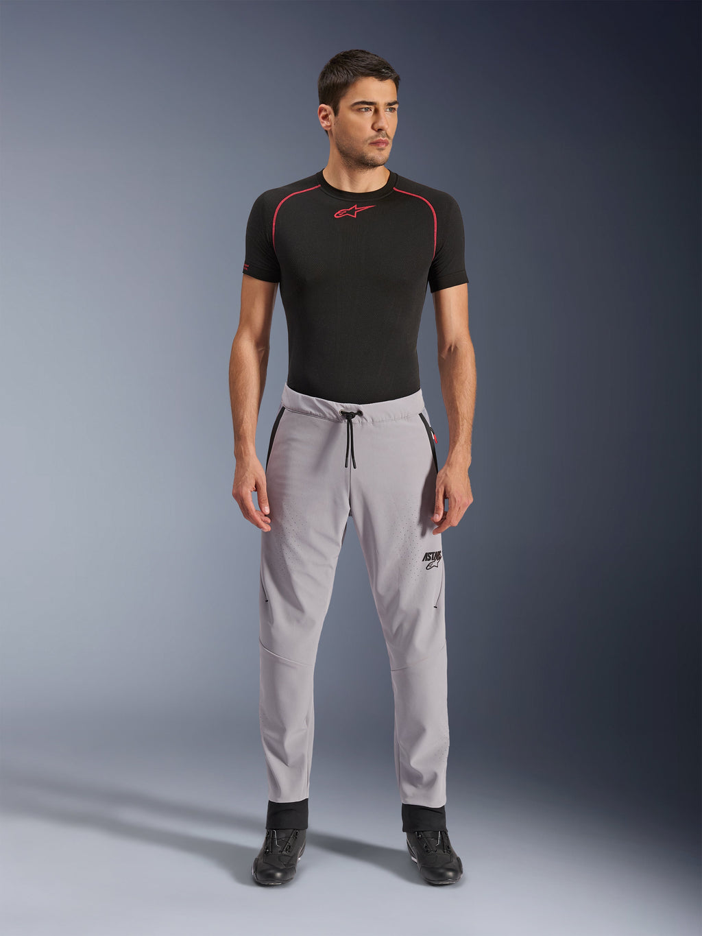 Alpinestars Aeroshell Airflow-byxor, mellangrå, lätta textilbyxor med laserperforerade ventilationszoner och dragsko i midjan, bärs av en modell med en svart kompressionströja och svarta motorcykelstövlar, ren och modern sportig design