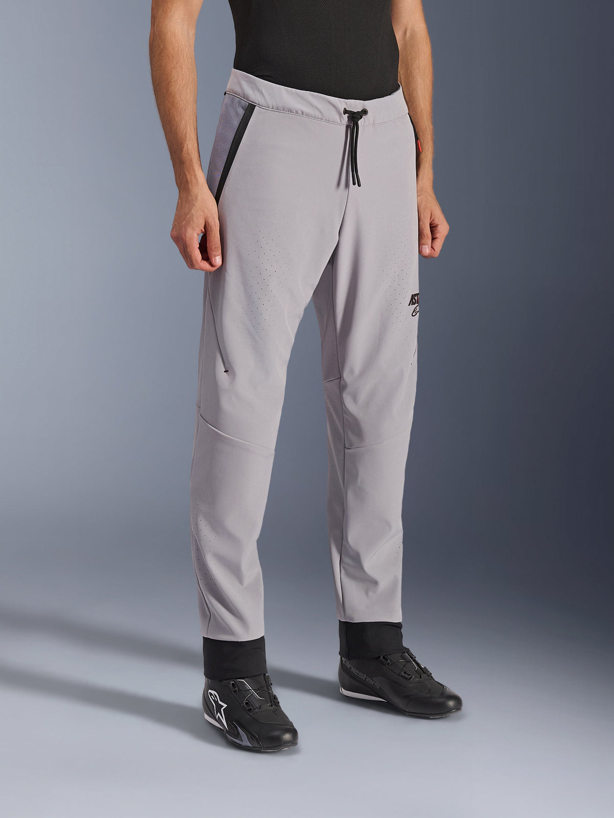 Alpinestars Aeroshell Airflow Pants, Mid Gray, lätta motorcykelbyxor med laserperforerade ventilationszoner på lår och smalben, elastiskt midjeband med dragsko och smal sportig passform, visas på en modell som bär svarta körskor.