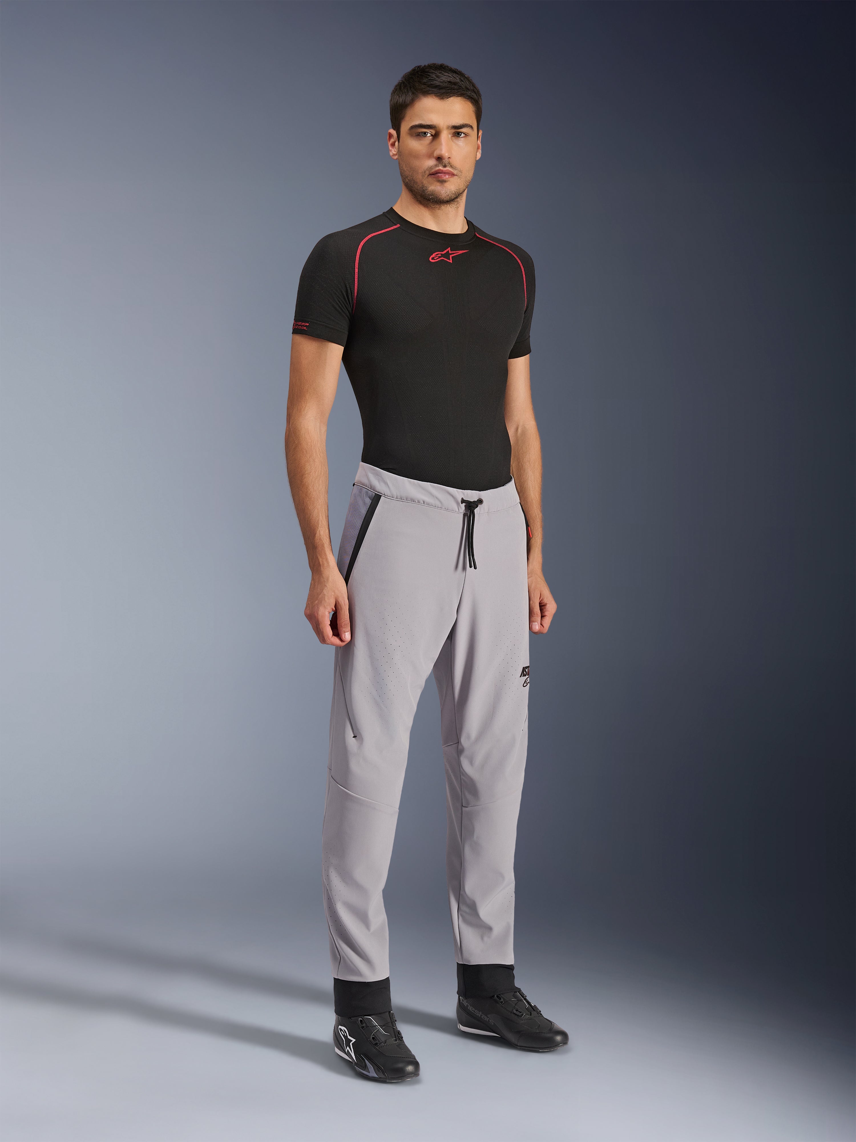 Alpinestars Aeroshell Airflow-byxor, motorcykelbyxor, mellangrå, bärs av en modell med en svart teknisk t-shirt och svarta mc-skor, med laserperforerade ventilationszoner, elastiskt midjeband med dragsko och en strömlinjeformad sportpassform.