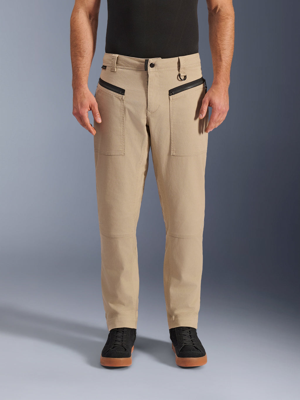Alpinestars Flex-AST Canvas-byxor, urbana motorcykelbyxor, bruna, klassisk arbetsklädesstil, med svarta horisontella framfickor med dragkedja och D-ring på bältesöglan, bärs med svart tröja och skor, studiobild framifrån