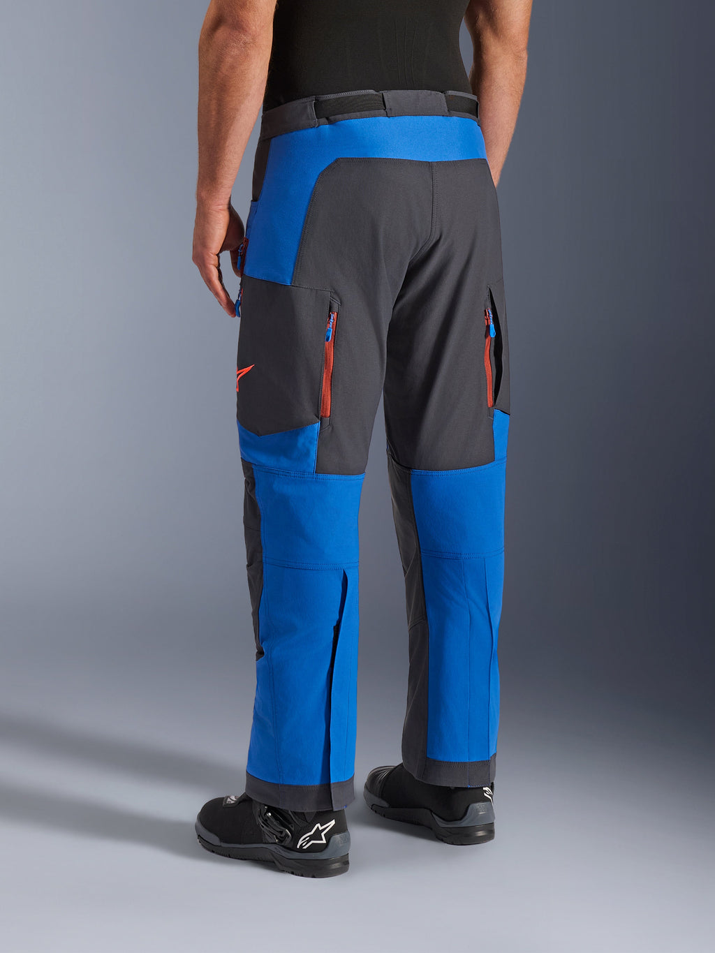 Alpinestars Maxdura Dual-byxor, kungsblå och mörkgrå, vy bakifrån som visar fickor med dragkedja och ventilationszoner, design för körning över stövlar bärs med svarta Alpinestars-stövlar, slitstark utrustning för äventyrs- och dual-sport-körning