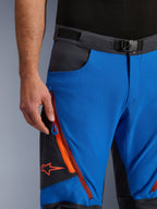 Alpinestars Maxdura Dual byxor i kungsblå och mörkgrå, närbild av midjebandet med magnetspänne, benficka med dragkedja med orangea detaljer och röd Alpinestars-logotyp, teknisk MC-utrustning för äventyrsåkning