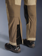 Alpinestars Maxdura Dual Pants i Walnut Aluminum, detaljerad vy av underben och nederkant med en over-the-boot-design, justerbara kardborrestängningar och förstärkta innerpaneler, matchade med svarta motorcykelstövlar.