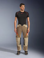 Alpinestars Maxdura Dual byxor, äventyrs- och dual-sport-byxor, Walnut Aluminum, bärs med en svart kortärmad kompressionströja och äventyrsstövlar, med orangea ventilationsöppningar med dragkedja och röda logotyper på låren, svart midjebälte med spänne, designade för att bäras över stöveln för motorcykelkörning.