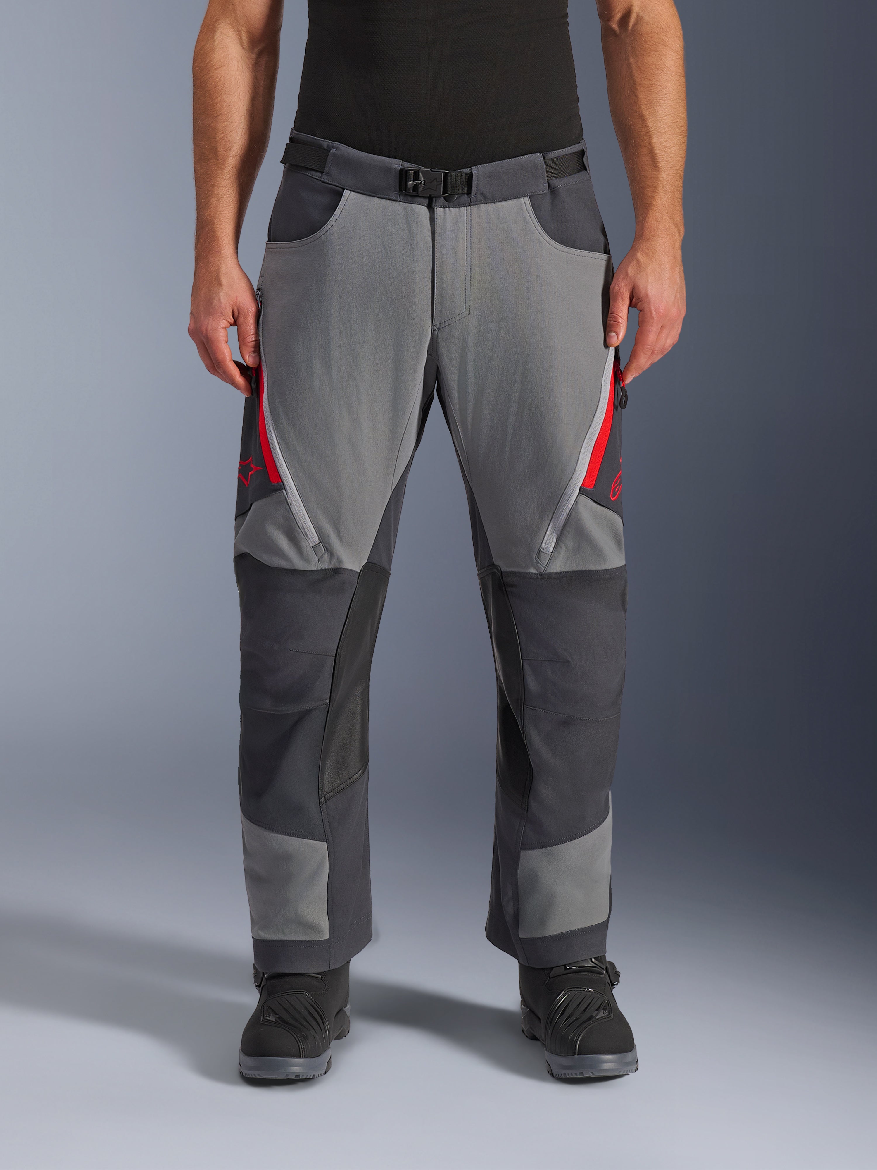 Alpinestars Maxdura Dual-byxor, adventure-motorcykelbyxor, mörkgrå och djupt grå med röda detaljer, vy framifrån som visar lårventilation med dragkedja, bälte med magnetspänne och förstärkta knäpaneler, design för att bäras över stövlar för dual-sport-körning