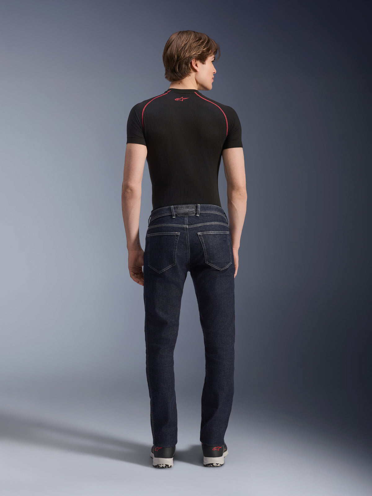 Alpinestars Copper V3 Denim-byxor i Rinse Blue, urbana motorcykeljeans sedda bakifrån, med rak passform (regular fit) och bakfickor, bärs med en svart kortärmad topp och sneakers.