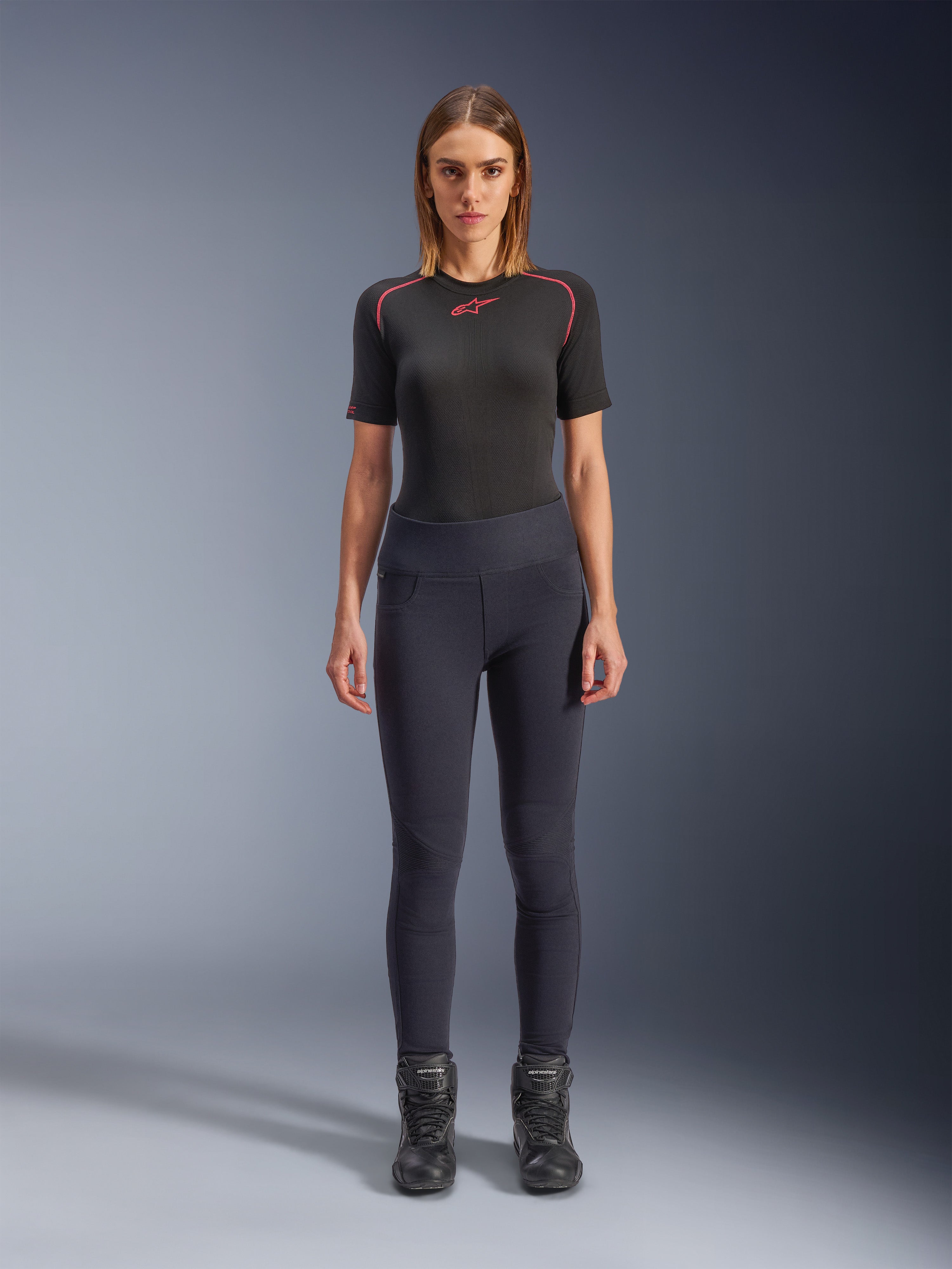 Alpinestars Stella Flex-AST Leggings, women's urban motorcycle leggings in Black, skinny high-waisted design worn with a black short-sleeve technical top and black riding boots, featuring accordion knee panels and a contemporary minimalist look