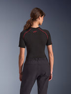 Kvinna i Alpinestars Stella Flex-AST Explorer Pants, svarta mc-byxor för äventyr, vy bakifrån, kombinerat med en svart kortärmad topp med röda sömmar, som framhäver den andningsbara textilkonstruktionen och det elastiska midjebandet.