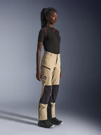 Alpinestars Woman Stella Flex-AST Explorer Pants, Sand and Black adventure touring pants, side profile on a model wearing a black Alpinestars t-shirt and riding boots, featuring ripstop knee reinforcements and zippered cargo pockets.