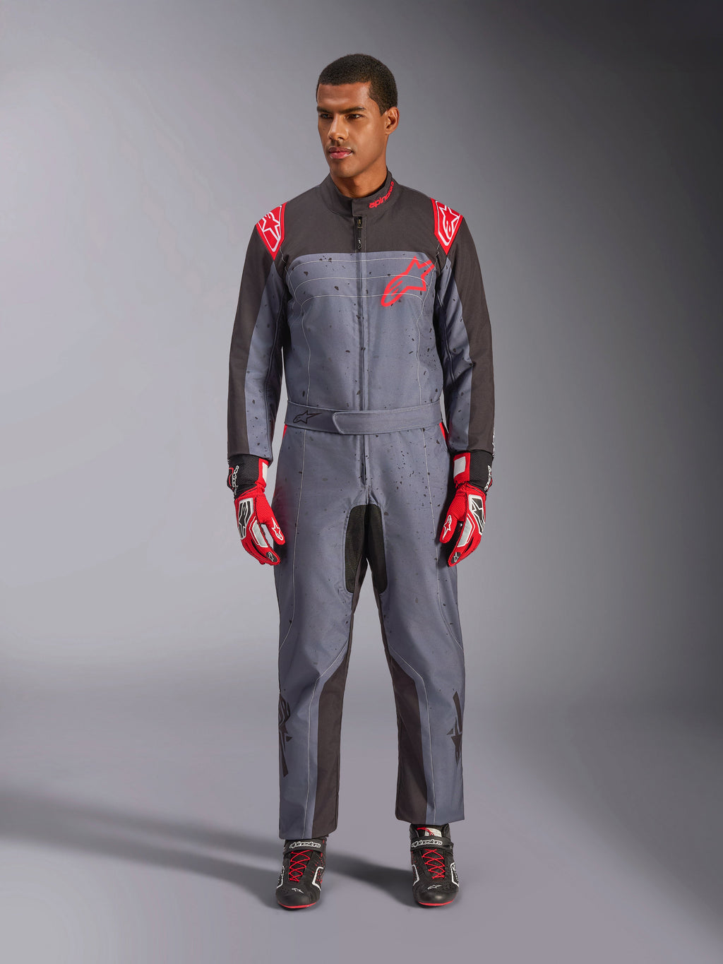 Alpinestars KMX-9 V3 Graphic 6 Suit, kartingdräkt, antracit, svart och röd, grått spräckligt grafiskt mönster, svarta paneler på insidan av armar och ben, röda Alpinestars-logotyper på axlar och bröst, bärs med röda racinghandskar och svarta skor