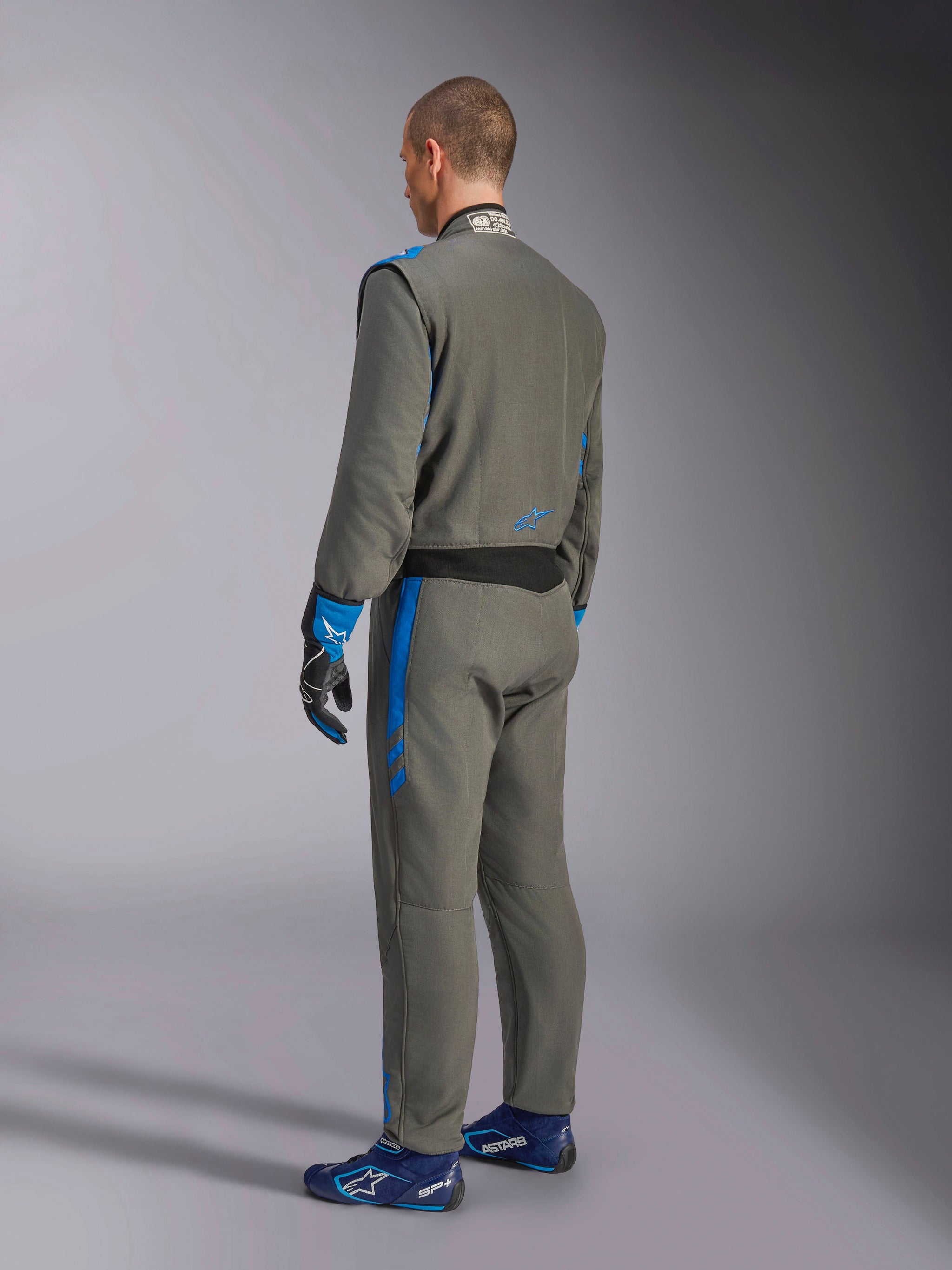Alpinestars GP Race V3 Suit FIA, bilsportoverall, Anthracite Blue, baksida av modell som bär den grå racingoverallen med blå detaljer, matchande blå handskar och racingskor, professionell design för motorsportutrustning
