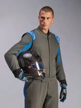 Manlig förare i Alpinestars GP Race V3 Suit FIA i Anthracite Blue, håller en racinghjälm i kolfiber med ett iriserande visir, professionell racingutrustning med blå axeldetaljer och matchande racinghandskar.