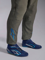 Alpinestars GP Race V3 Suit FIA, antracitblå racingoverall, närbild av underbenen med en blå broderad Astars-logotyp vid ankeln, matchad med marinblå och cyanfärgade racingskor, professionell skyddsutrustning för motorsport