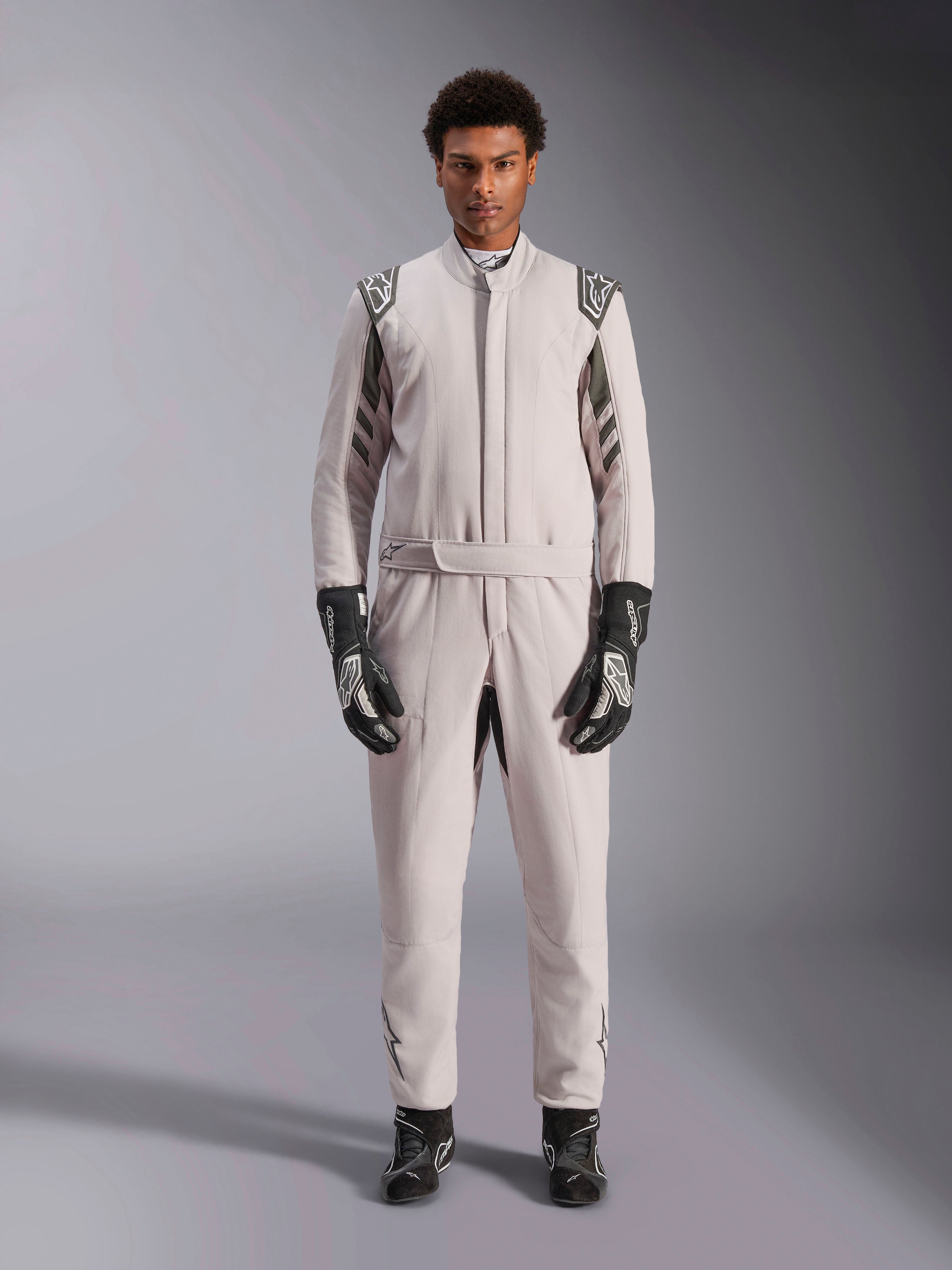 Alpinestars GP Race V3 Suit FIA i Silver Anthracite, racingoverall för bilsport i ett stycke som bärs av en modell, med mörkgrå axelklaffar och detaljer, kombinerad med svarta racinghandskar och stövlar, professionell skyddsutrustning för motorsport.