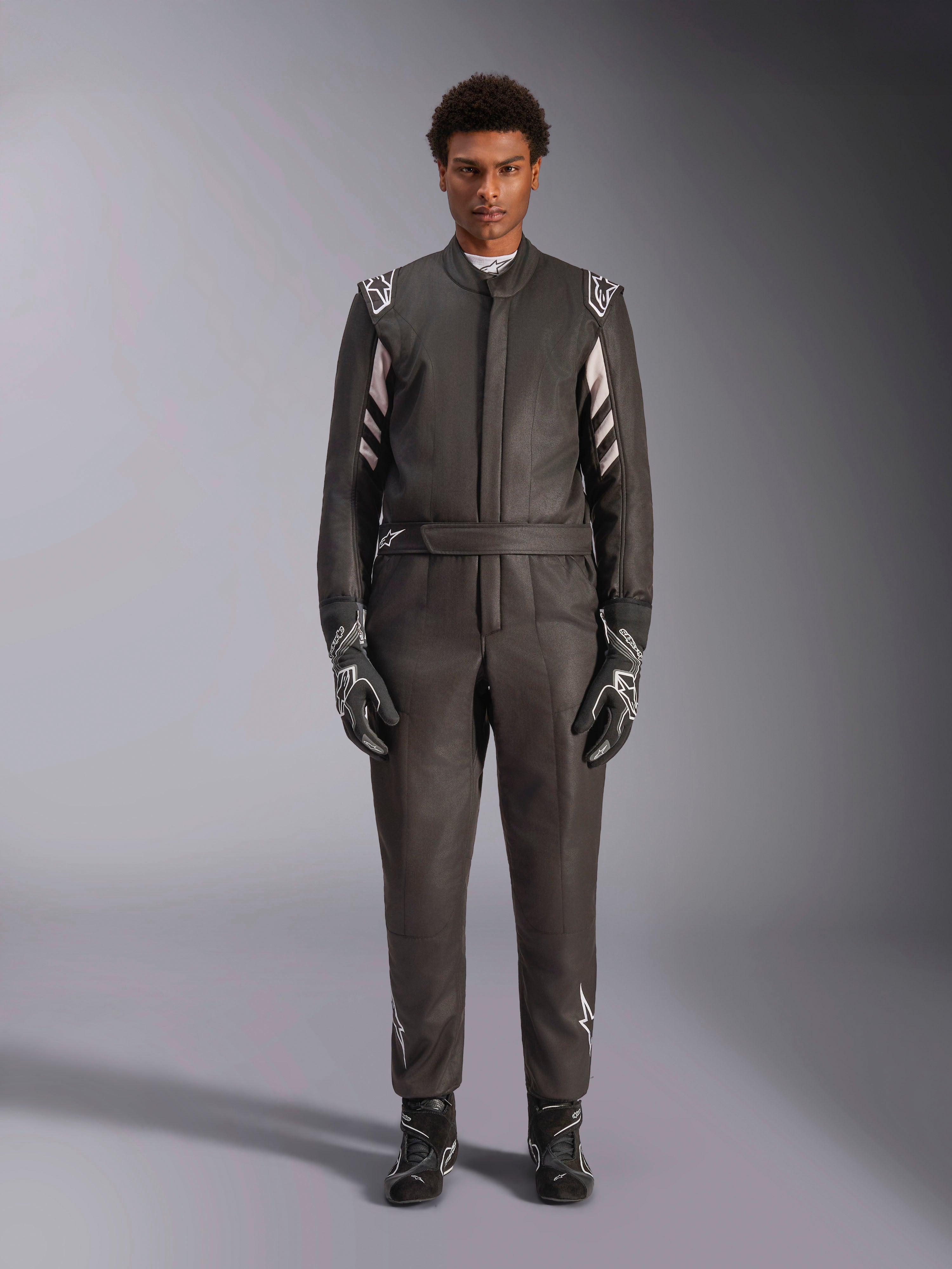 Alpinestars GP Race V3 Suit FIA, racingoverall för bil, svart och silver, frontvy av förare klädd i komplett racingutrustning inklusive handskar och skor, professionell motorsportdesign med Alpinestars-logotyper på axlar och bälte