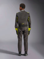 Alpinestars GP Race V3 Suit FIA, vy bakifrån, svart med neongula detaljer, med gula paneler på armarna och överkroppen, gul logotyp på nedre delen av ryggen, bärs med matchande racinghandskar och stövlar, professionell racingoverall för bilsport.