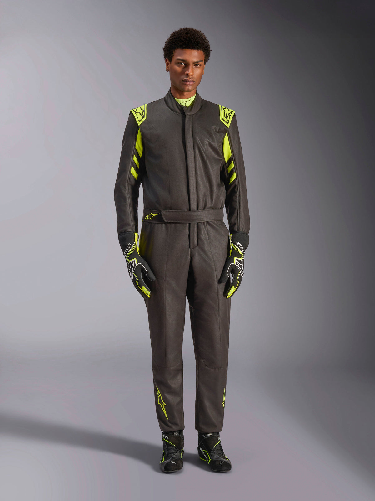 Alpinestars GP Race V3-overall FIA, föraroverall för bilracing, svart och fluorescerande gul, bärs av en modell med matchande racinghandskar och skor, med neongula detaljer på axlar, midja och ärmar, professionell motorsportutrustning