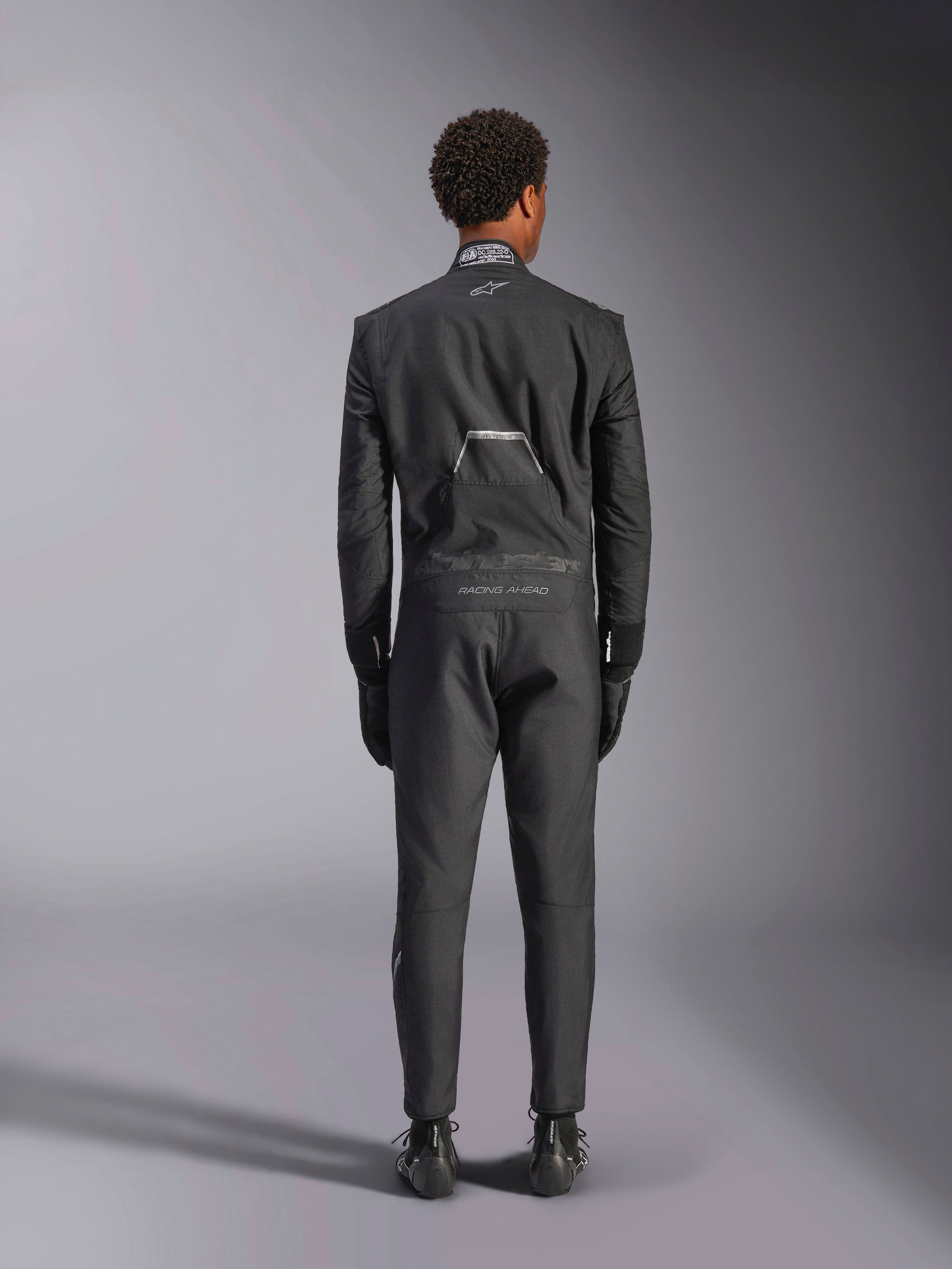 Alpinestars Hypertech V3 Suit, Black Dark Shadow, baksida av en professionell racingoverall i ett stycke för bilracing, med FIA-certifieringsetikett på kragen och "Alpinestars" och "RACING AHEAD"-märkning på ländryggen, bärs med matchande svarta racinghandskar och stövlar.