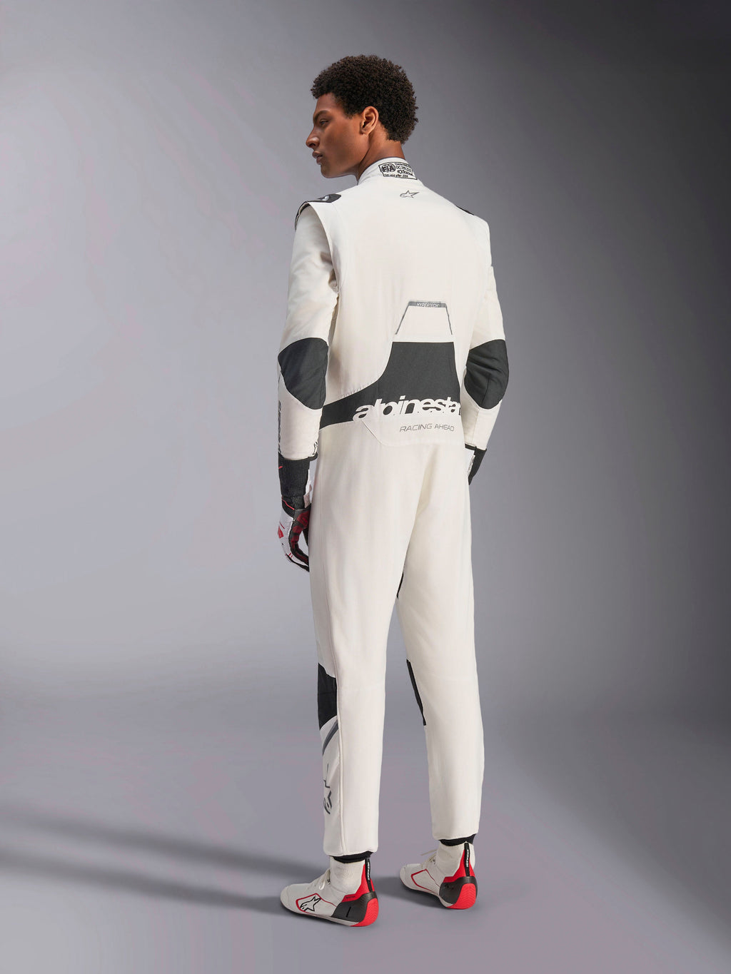 Alpinestars Hypertech V3-dräkt, professionell racingdräkt, vit, svart och silver, baksida av modell som visar svarta stretchpaneler på ländryggen och armbågarna, Alpinestars-logotyp på ryggen, kombinerad med matchande racinghandskar och racingskor för en komplett motorsportlook