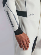 Alpinestars Hypertech V3 Suit, närbild på vit racingoverall med svarta och silverfärgade detaljer, Alpinestars-logotyp på underarmen, svart stickad mudd vid handleden och mörka stretchpaneler för rörlighet, professionella motorsportkläder.