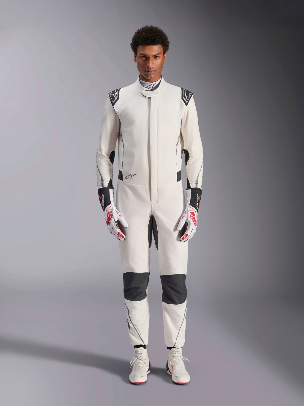 Alpinestars Hypertech V3-dräkt, professionell racingdräkt för bilsport, vit, svart och silver, bärs av en modell med röd-vita handskar och matchande vita racingskor, med svarta kontrastpaneler och Alpinestars-logotyper, atletisk slim fit-design