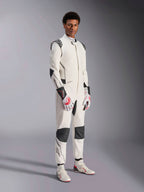 Manlig modell i Alpinestars Hypertech V3 Suit, vit med svarta och silvriga detaljer, professionell bilracingutrustning med svarta paneler på axlar och knän, matchad med vita och röda racinghandskar och vita racingstövlar