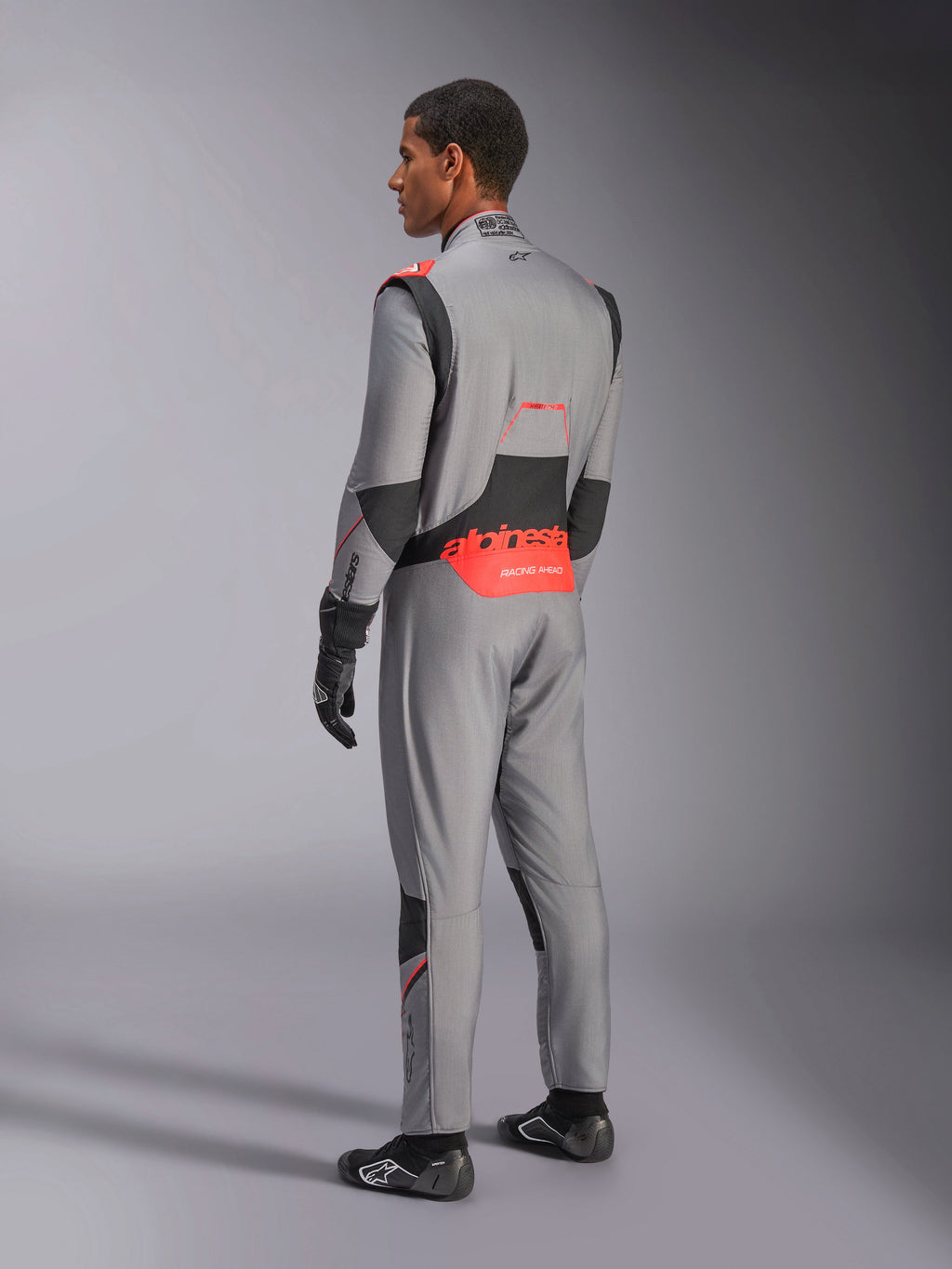 Alpinestars Hypertech V3-dräkt i Mid Gray Black Red Fluo, trekvartsvy bakifrån, med framträdande röd Alpinestars-logotyp på ländryggen, svarta stretchpaneler och en smidig atletisk passform för professionell bilsport.