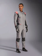 Manlig modell som bär Alpinestars Hypertech V3 Suit i Mid Gray med svarta och Red Fluo-detaljer, professionell racingoverall kombinerad med svarta racinghandskar och skor, med en lättviktskonstruktion i två lager Nomex, röda axeldetaljer och atletisk passform.