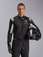 Manlig modell i Limited Edition Lamborghini GP Tech V4-dräkt, svart racingdräkt med silverfärgade detaljer och Lamborghini Squadra Corse-logotyp, håller en kolfiberhjälm, svarta racinghandskar med vita logotyper, professionell racingutrustning