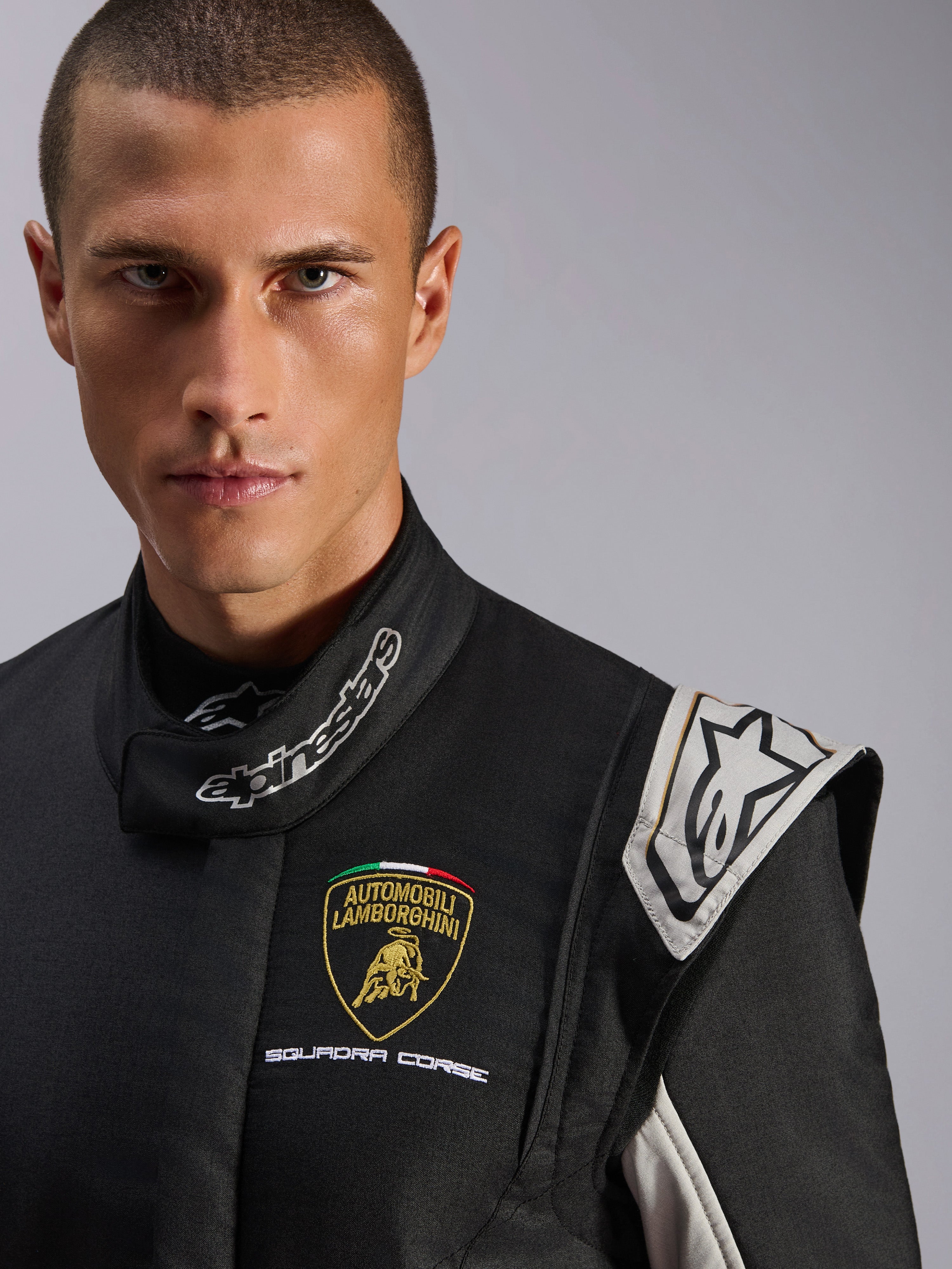 Alpinestars Limited Edition Lamborghini GP Tech V4 Dräkt, professionell racingdräkt, svart med detaljer i silver och guld, närbild med Lamborghini Squadra Corse-logotyp på bröstet och Alpinestars-branding på kragen, premiumskydd för motorsport