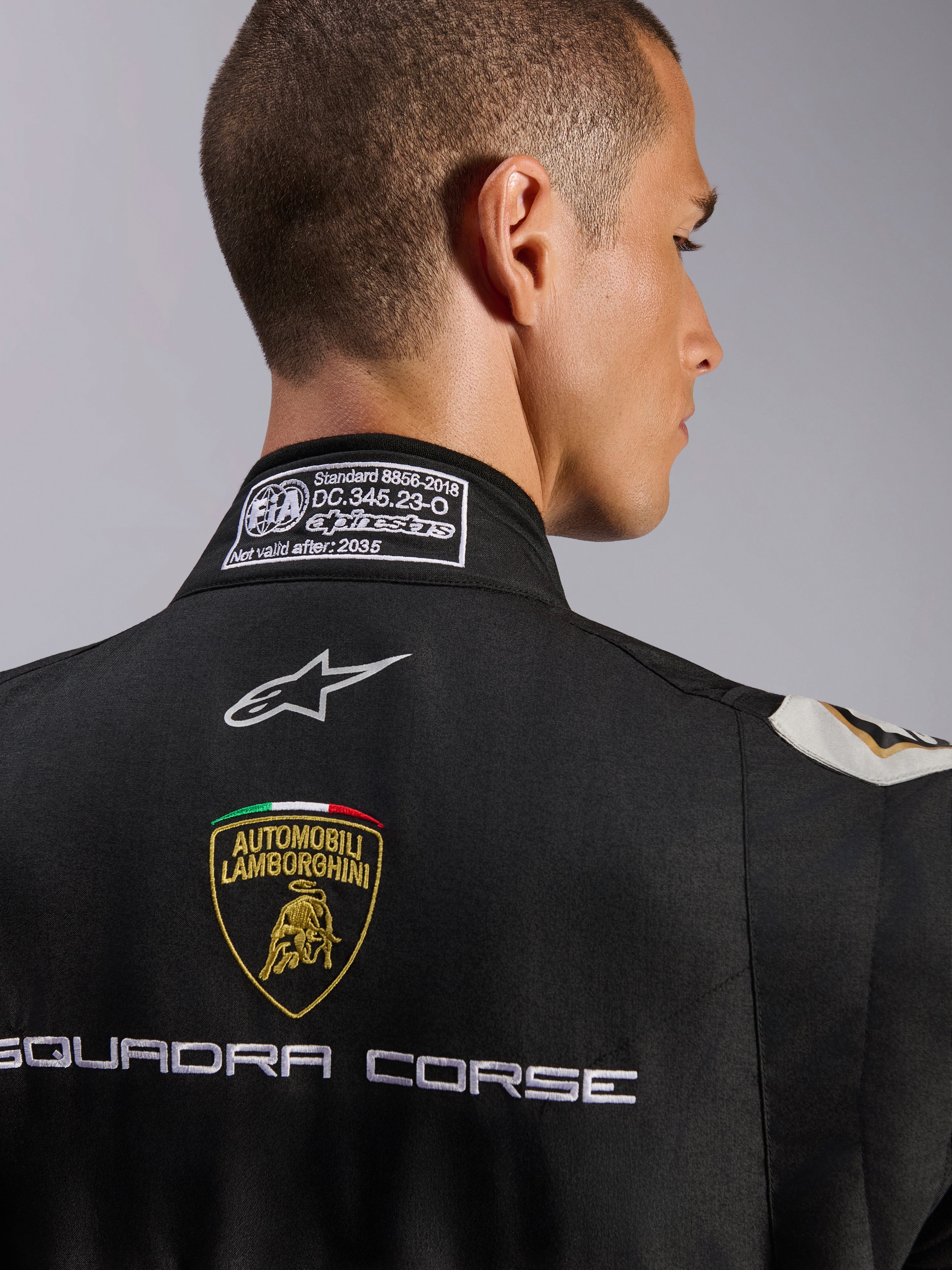 Alpinestars Limited Edition Lamborghini GP Tech V4-dräkt FIA, närbild av övre ryggen och kragen, svart dräkt med Automobili Lamborghini-sköld och Squadra Corse-broderi, Alpinestars-logotyp och FIA 8856-2018-certifieringsetikett på kragen.