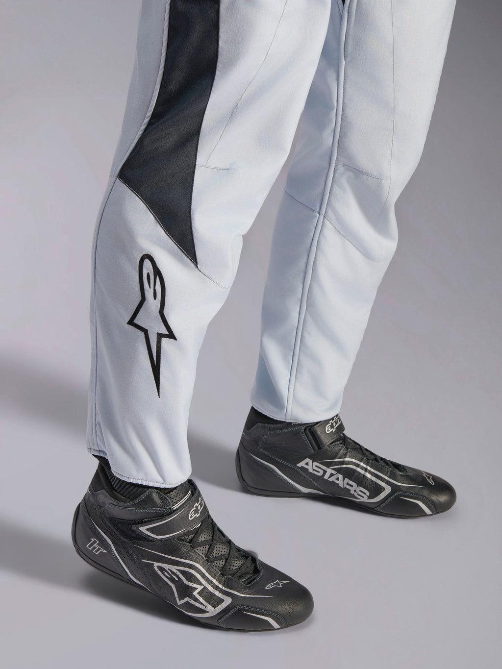 Alpinestars GP Pro Comp V2 FIA racingoverall, grå och svart med stjärnlogotyp på benet och matchande svarta racingstövlar.